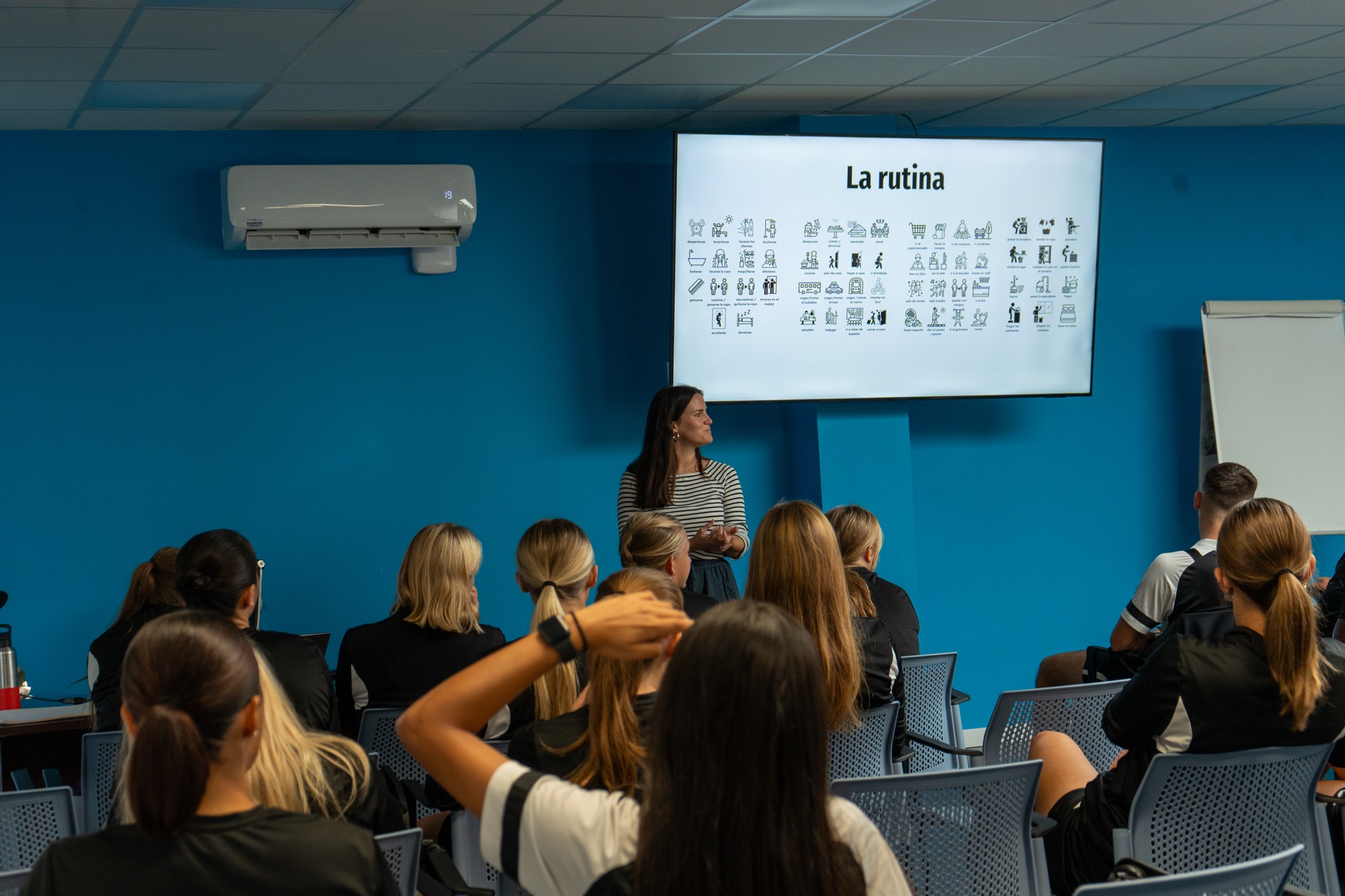 Una profesora da una clase de español a jugadores y jugadoras de la academia