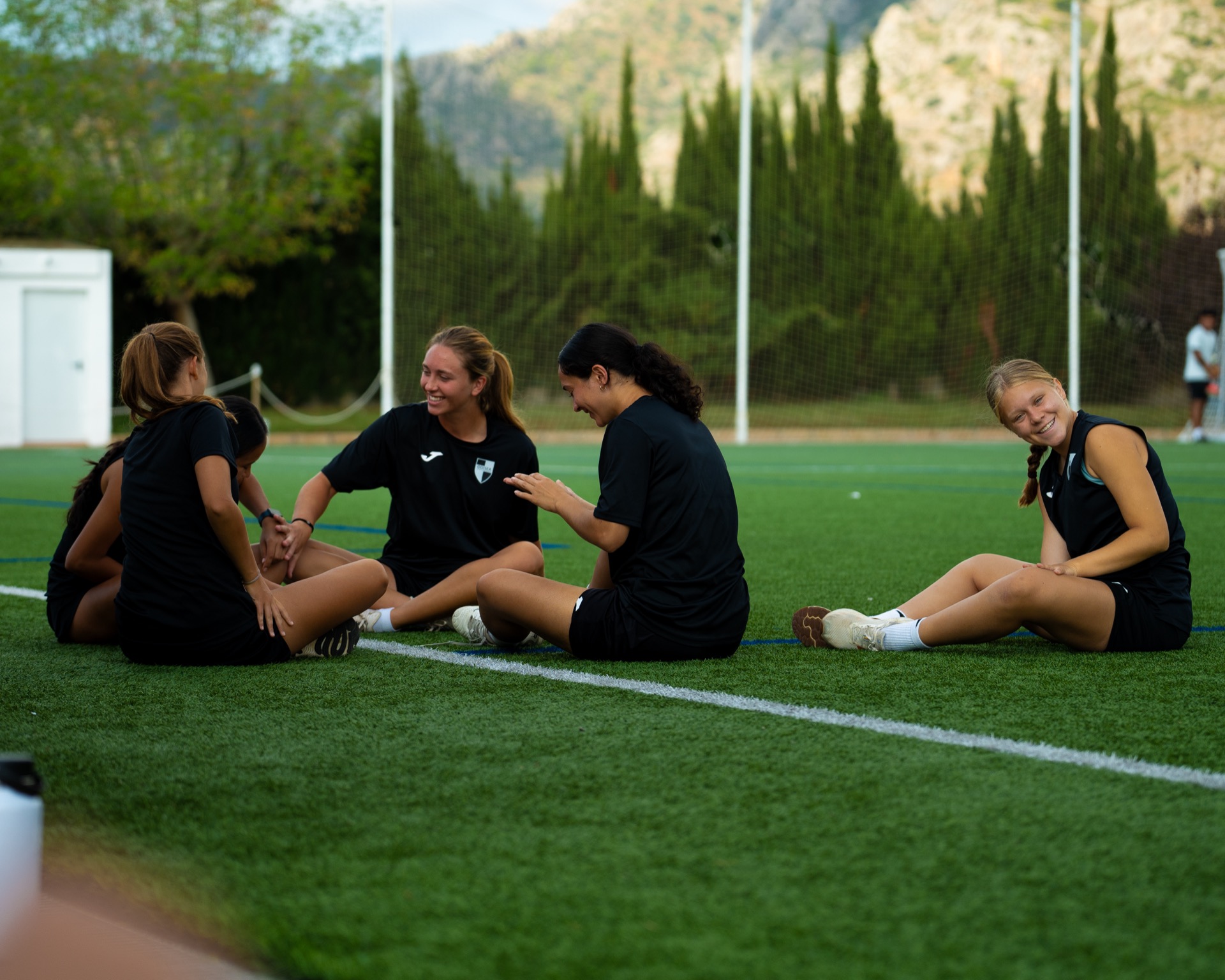 Jugadoras de la academia femenina sentadas en el césped, charlando y riendo después del entrenamiento